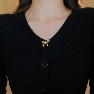 Detail view of gold bow brooch with pearl on a black ribbed knit sweater neckline