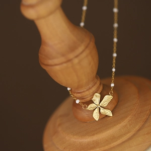 18K gold plated flower necklace with white beads and brushed metal petals on wooden stand