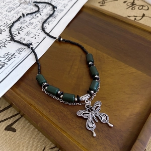 Detail of a ceramic butterfly pendant with green beads and black chain on a vintage tray