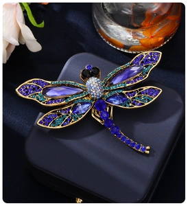 Close-up of vintage dragonfly brooch with blue rhinestones and purple gems on a jewelry box
