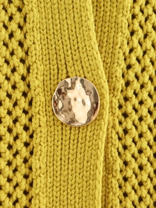 Dettaglio della trama in maglia grossa giallo senape con un bottone in metallo dorato