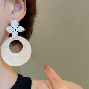 Detail view of floral stud earring with large resin ring on model in neutral lighting