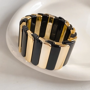 Macro detail of wide elastic bracelet featuring alternating black enamel and gold metal blocks