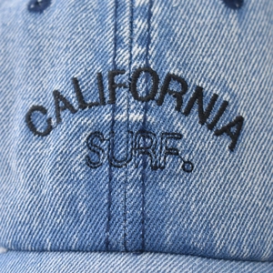 Macro view of CALIFORNIA SURF embroidery on blue washed denim baseball cap