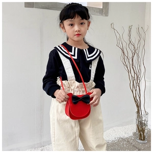 Detail of red child crossbody bag with round ears and a black bow in a studio setting