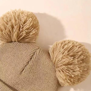 Detail shot of the camel double pom-pom knit beanie showing texture and ribbed knit fabric