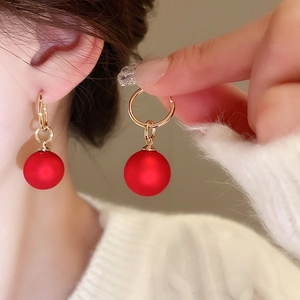 Detail of gold hoop earrings with red matte ball pendants for Lunar New Year style