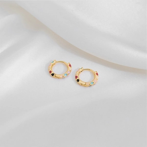 Macro detail of gold hoop earrings with vibrant colorful enamel dots on white silk