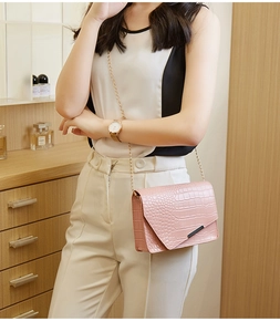 Detail of pink croc-embossed small crossbody bag with gold chain and asymmetrical flap