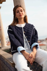 Detail of navy blue quilted jacket with white contrast piping and striped sleeve lining
