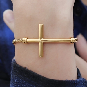 Bracelet croix en acier inoxydable doré au poignet avec détails de chaîne tressée élégants