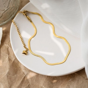 Elegant gold snake chain necklace with a heart pendant on white ceramic plate