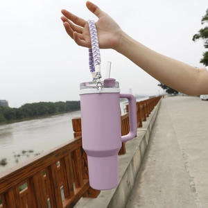 Detail showing hand holding 40oz purple insulated tumbler with woven handle strap