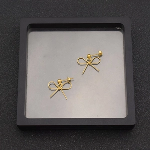 Detailed macro view of gold-plated minimalist bow earrings in a black display case