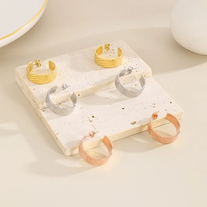 Detail of C-shaped textured earrings in gold, silver and rose gold on stone pedestal