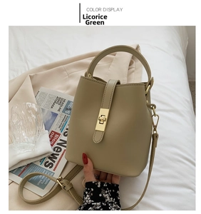 Detail of licorice green bucket bag with golden twist lock on a white linen background