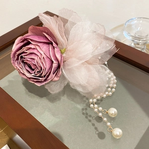 Detailed view of lace rose hair clip with elegant pearl tassels on a wooden surface