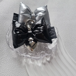 Silver and black puffy bow keychains with heart charm on a textured glass tray