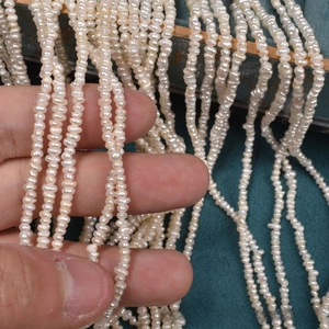 Macro view of 2-3mm mini natural freshwater pearls string on dark velvet background