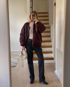 Close-up of a burgundy oversized bomber jacket styled with a white striped knit sweater
