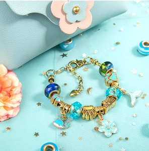 Detail of blue glass beads and ocean-themed pendants on a gold DIY charm bracelet