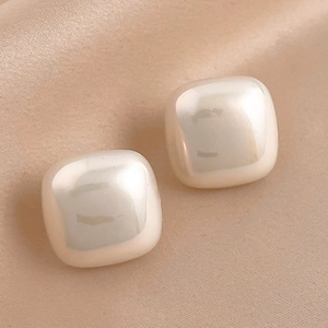 Close-up of geometric square pearl earrings on champagne silk fabric texture