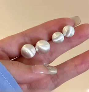 Close-up of minimalist brushed metal round earrings with fine texture shown in hand