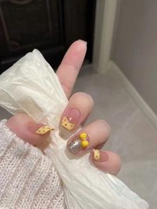 Detail of yellow press-on nails with 3D bow accent and silver glitter dots decoration