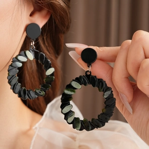 Detail of twisted black hoop earrings featuring green marbled stone inlay inserts