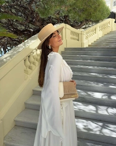 Detail of beige woven flap bag with gold metal logo and white ruffle chiffon dress