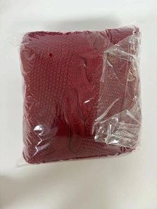 Detail of red knit Christmas tree skirt with white pom poms folded in plastic packaging
