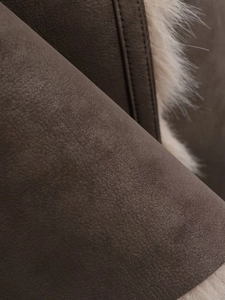 Détail de suède marron foncé et doublure en fausse fourrure crème sur un manteau d'hiver