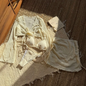 Dettaglio bikini 4 pezzi all'uncinetto color crema con copricostume in rete su tappeto