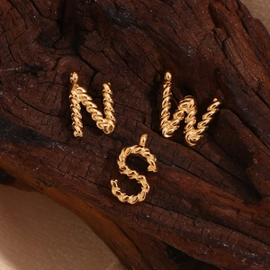 Close-up of golden alphabet pendants N W S with twisted rope texture on dark wood