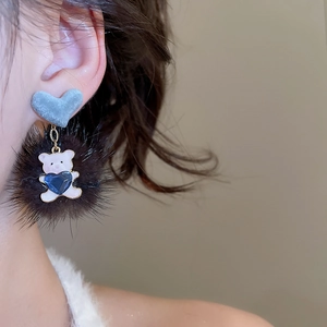 Close-up of heart stud earring with black pompom and cute white bear charm detail