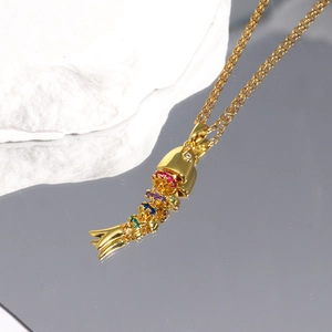 Macro detail of a flexible gold-plated fish pendant with vibrant multi-color gemstones