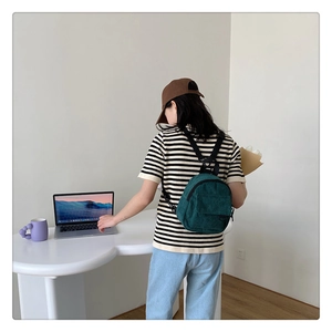 Dark green corduroy mini backpack for women styled on a desk with laptop and decor
