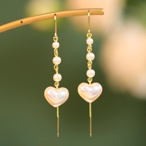 Macro shot of long tassel pearl earrings with an iridescent heart pendant and gold chain