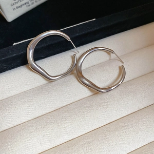Macro shot of silver irregular twisted hoop earrings resting in a beige textured jewelry box