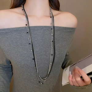 Multi-layer long necklace with black and silver beads layered on a grey off-shoulder top