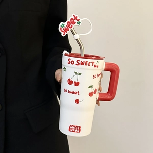 Detail of white ceramic mug with red cherry patterns, handle, and sweet straw decoration