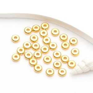 Flat lay of 14k gold plated spacer beads with sea shell and white ribbon on fabric