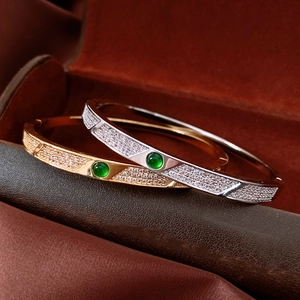 Detail of 18K gold and silver plated bangles with green gems and inlaid zircons