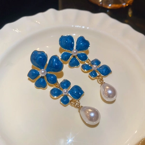 Detail view of blue enamel flower earrings with elegant teardrop pearls on a plate