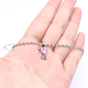Silver devil heart necklace with pink zircon gemstone held in a hand on white background