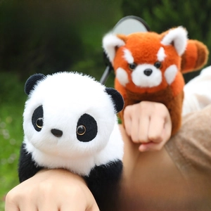 Close-up of plush red panda slap bracelets on wrist with soft outdoor lawn background