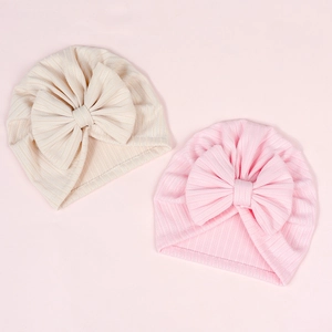 Flat lay of pink and beige newborn hats with large bows and ribbed texture detail