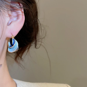 Close-up of model wearing blue enamel gold twisted hoop earrings for office style