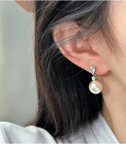 Détail d'élégante boucle d'oreille argentée avec zircon goutte et perle dorée champagne