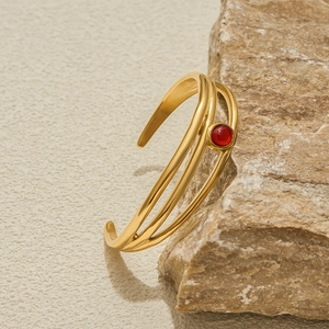 Dettaglio macro di un bracciale a tre strati in acciaio dorato con pietra rossa